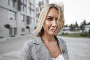 Portrait of young blonde businesswoman in gray suit walking in the city