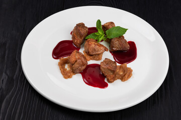Delicacy Fried pork meat with zucchini puree and berries sauce decorated with mint on white plate on black wooden background