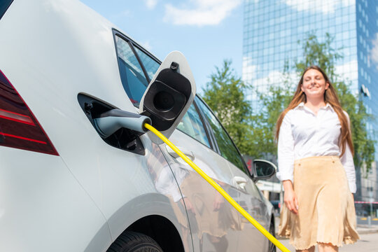Smiling woman unplugging the electric car charger at a downtown charging point