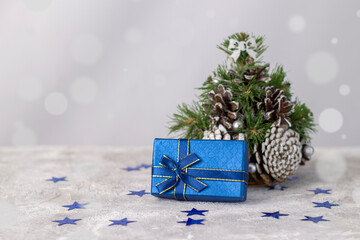 Gift blue box with blue ribbon near christmas tree on gray background with bokeh