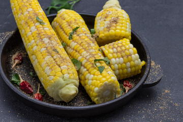 Boiled corn sprinkled with powdered seasoning pods of red pepper in frying pan