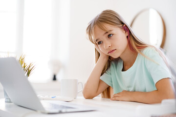 Obraz premium Happy little girl pupil using laptop at home