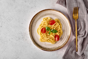 Spaghetti pasta with tomato cherry, parmesan cheese and basil on ceramic plate with fork and napkin on gray background. Copy space for text