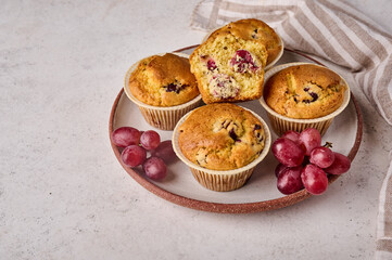 Homemade cupcakes with cherries and grapes on plate with napkin on light background, close up