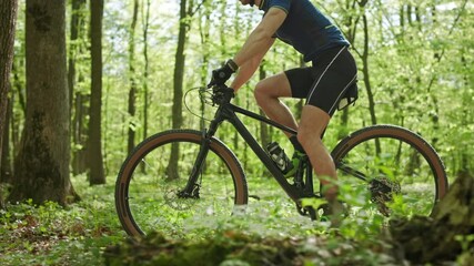 A man on an MTB bike is riding through the forest. He is training before the competition. The camera is shooting from the side and moving with him. 4K - Powered by Adobe