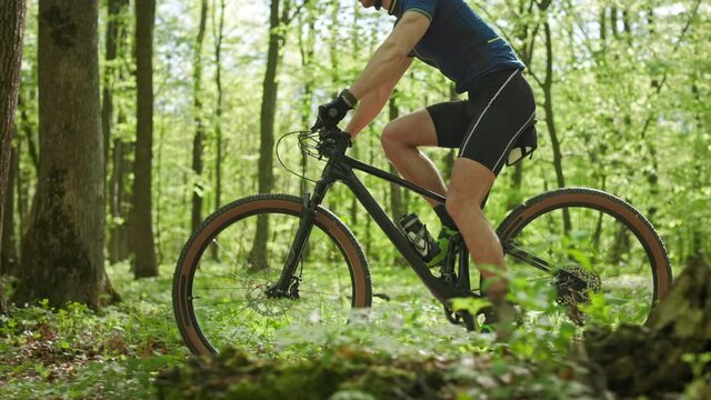 A man on an MTB bike is riding through the forest. He is training before the competition. The camera is shooting from the side and moving with him. 4K