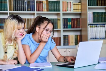 Two girls, students, adolescents 15, 16 years old study in library, using laptop