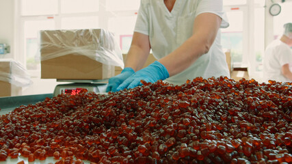 Candy factory. Factory worker packing candies. Young woman in uniform using scoop to put jelly...