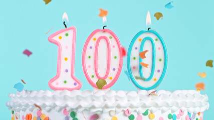 Colorful tasty birthday cake with candles shaped like the number 100. Pastel blue background.
