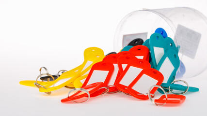 A branch of metal ring key chain attached with red black yellow and green plastic name tag with white cardboard paper inside next to the clear plastic cylinder box. Isolated on white background