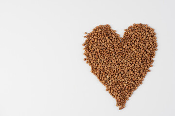 Raw buckwheat groats on a white background in the shape of a heart sing. Valentine's Day concept. Copy space place. Fried buckwheat heart isolated. Image cut and placed on white background. 