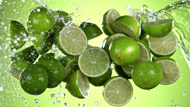 Fresh limes flying with water splashes on green gradient background