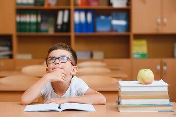 Concentrated schoolboy sitting at desk and writing in exercise book with classmate sitting behind
