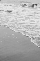 Sea waves, sea water on the sand. The atmosphere of the sea and relaxation. Empty beach. Yellow sand. Sea view. Poster. Postcard. Black and white photography. Vertical photography of nature.