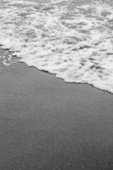 Sea waves, sea water on the sand. The atmosphere of the sea and relaxation. Empty beach. Yellow sand. Sea view. Poster. Postcard. Black and white photography. Vertical photography of nature.