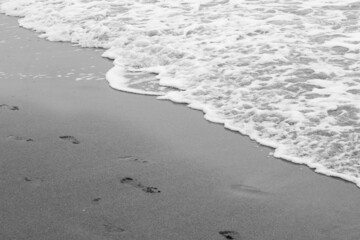 Sea waves, sea water on the sand. The atmosphere of the sea and relaxation. Empty beach. Yellow sand. Sea view. Poster. Postcard. Black and white photography. Vertical photography of nature.