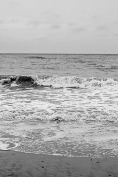 Sea waves, sea water on the sand. The atmosphere of the sea and relaxation. Empty beach. Yellow sand. Sea view. Poster. Postcard. Black and white photography. Vertical photography of nature.