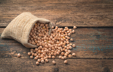 Dry chickpeas in a linen bag on a brown, wooden background.