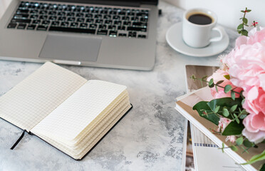 there is a laptop and a mug of coffee on the table, next to it lies a bouquet of flowers and magazines