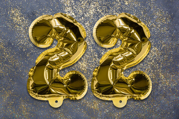 The number of the balloon made of golden foil, the number twenty two on a gray background with sequins. Birthday greeting card with inscription 22. Numerical digit, Celebration event, template.