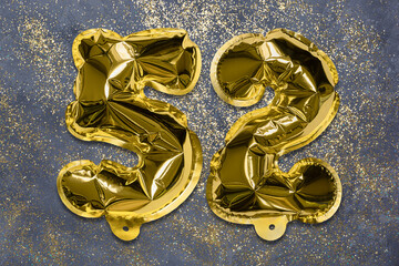 The number of the balloon made of golden foil, the number fifty-two on a gray background with sequins. Birthday greeting card with inscription 52. Numerical digit, Celebration event, template.