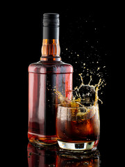 splash in a glass with whiskey from falling ice next to a bottle on a black background