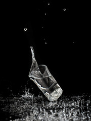 full falling shot glass with vodka or water with splashes on black background