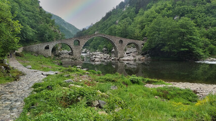 Fototapeta na wymiar Landscape with the Devil’s bridge in the Rhodope mountains in Bulgaria, an old ottoman monument which connected Thrace with Aegean Sea - spring medieval landscape with rainbow