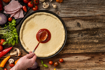 Raw delicious pizza dough with red souce on the wooden table