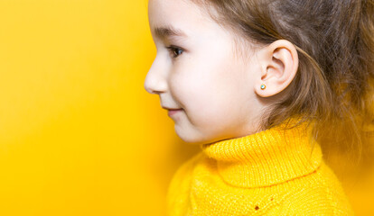 Ear piercing in a child - a girl shows an earring in her ear made of a medical alloy. Yellow...
