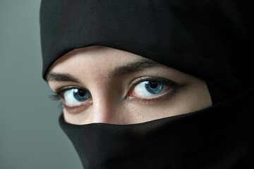 Naklejka premium The face of a young woman with large beautiful eyes, covered with a black Muslim veil. Close-up, selective focus.