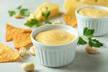 Cheese sauce and snacks on white textured table