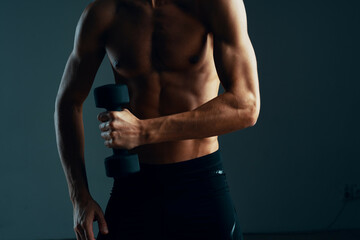Fototapeta na wymiar a man with a pumped up press workout with dumbbells exercises dark background