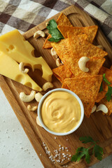 Board with cheese sauce and snacks on white textured table
