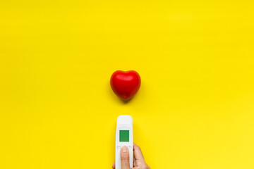 infrared thermometer and red heart on yellow background