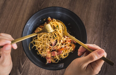 person's hand having spicy bacon pasta on table
