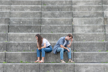 Relationship troubles concept with copy space. Sad and thoughtful couple sitting on stairs ignoring each other