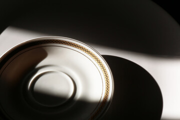 Piatto bianco e piattino da caffè decorato in oro. Composizione di due oggetti su fondo nero