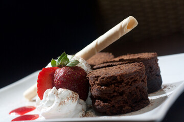 ice cream with slices of brownie cake with cherries and white cream and wafers served on a white plate
