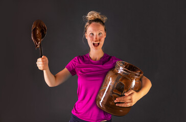 Frau mit großen Glas Schokoladencreme hält Löffel voller Schokolade in der Hand und freut sich