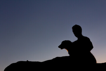 Silhouette of man playing with his dog at sunset. Backlight. Copy space.