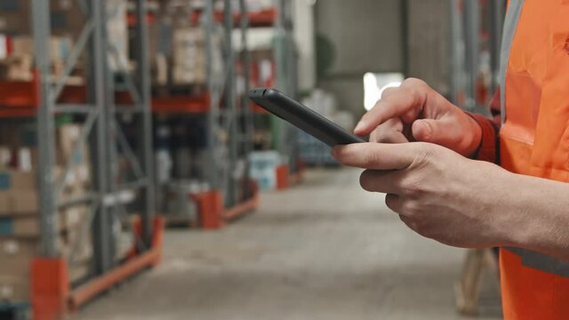 Handheld slowmo mid-section of unrecognizable male worker using mobile phone in warehouse