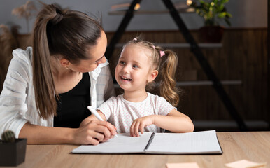 Caucasian young mother and little daughter sitting at the table in the evening, study online together