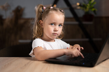 one little girl is sitting at a laptop in the evening and is typing. Portrait of a preschool child.