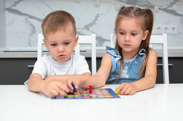 Fototapeta premium Board game and concept of children's leisure. Children have fun,laugh and have fun playing board game.They hold figures in their hands, red, blue, green chips. Boy and girl playing board game at home.