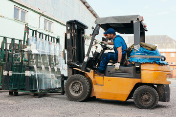 Worker driving forklift and loading glass constructions - obrazy, fototapety, plakaty
