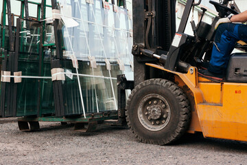 Close up of forklift wheel. Worker driving forklift and loading glass constructions
