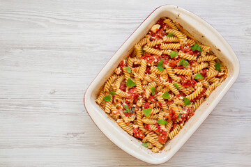 Homemade Baked Feta Tomato Pasta in a baking dish on a white wooden surface, overhead view. Flat lay, top view, from above. Copy space.