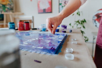 Female artist's hand sprinkling silver glitter on the fluid art picture