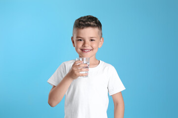 Cute little boy with glass of water on light blue background